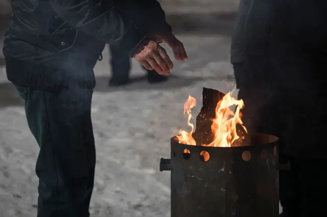 Люди зігріваються біля вогню в бочці на снігу взимку