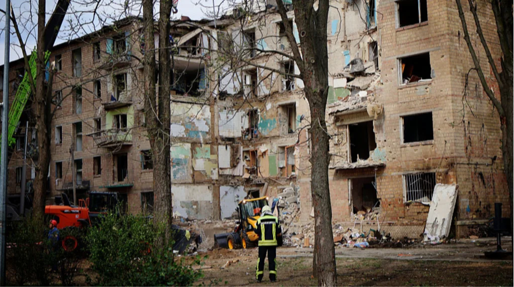 Пошкоджений багатоквартирний будинок з рятувальником на тлі руйнувань