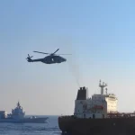 Вертоліт летить над морем біля танкера та військового корабля