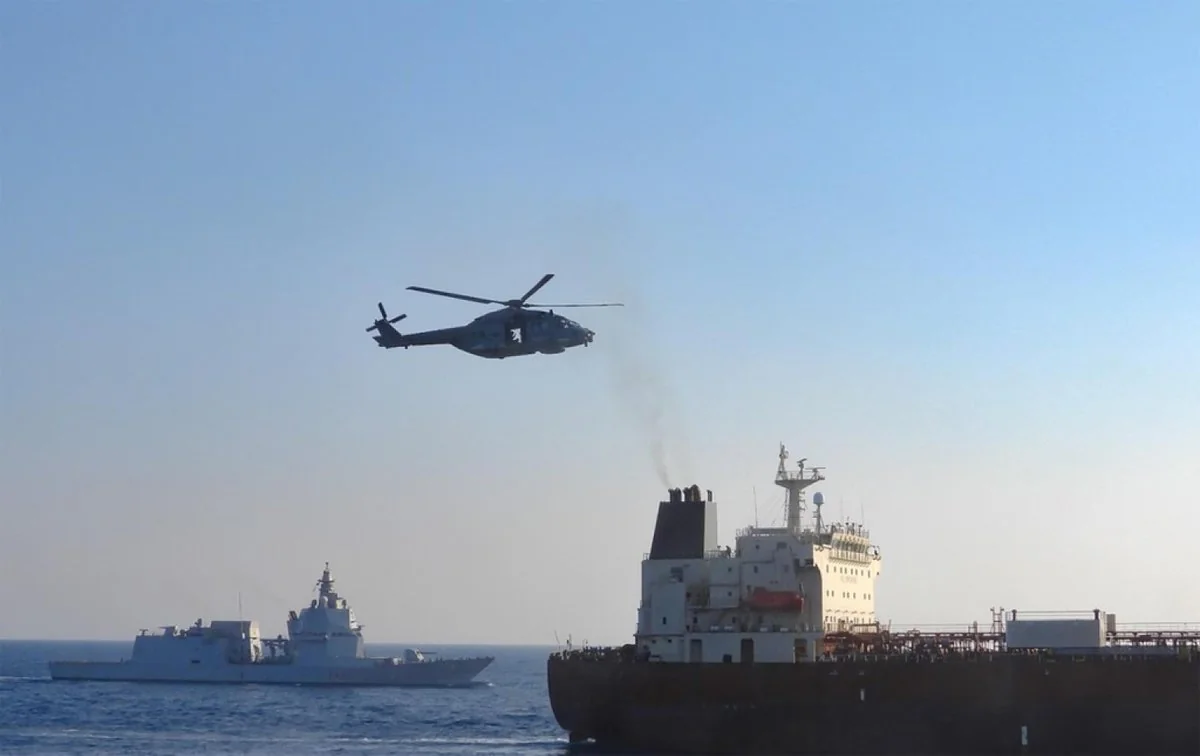 Вертоліт летить над морем біля танкера та військового корабля