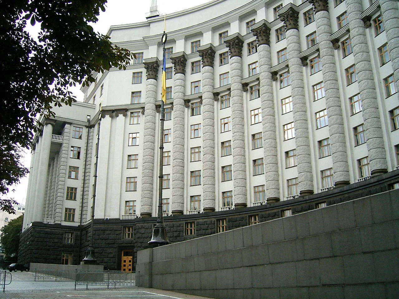 Фасад белого правительственного здания с колоннами и украинским флагом